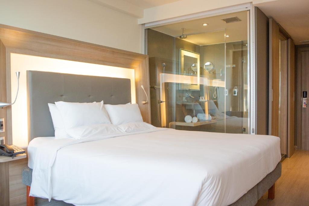 里约热内卢大西洋港诺富特酒店的卧室配有一张白色大床和玻璃墙