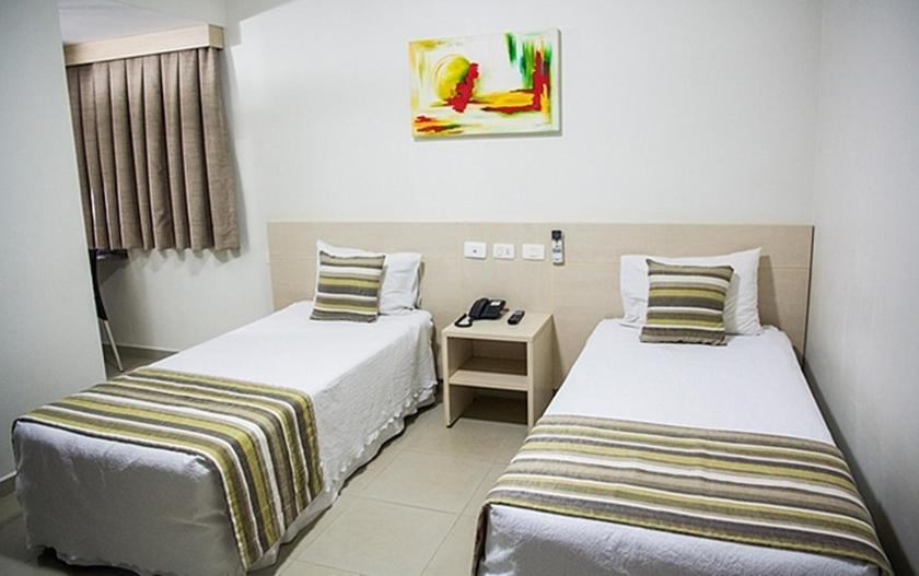 GoiatubaHotel Barrocos的酒店客房设有两张床和一张桌子。