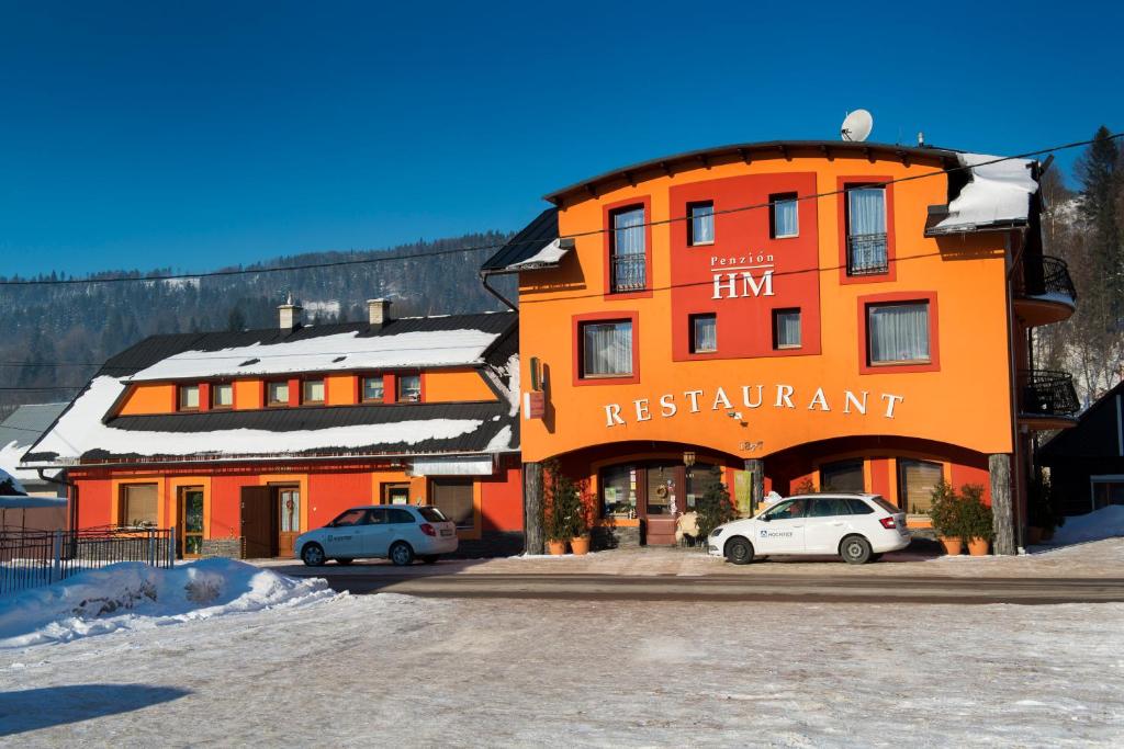 奥什恰德尼察HM膳食旅馆的一座橙色的建筑,前面停有两辆车