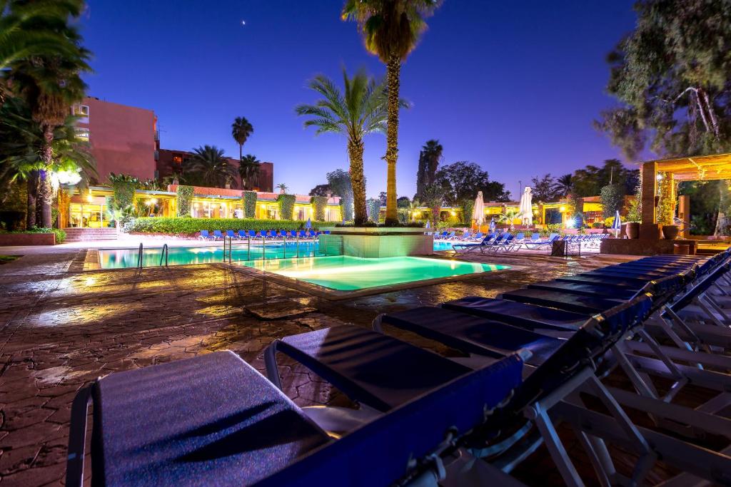 马拉喀什Kennedy Hospitality Resort的游泳池设有躺椅,晚上种植棕榈树