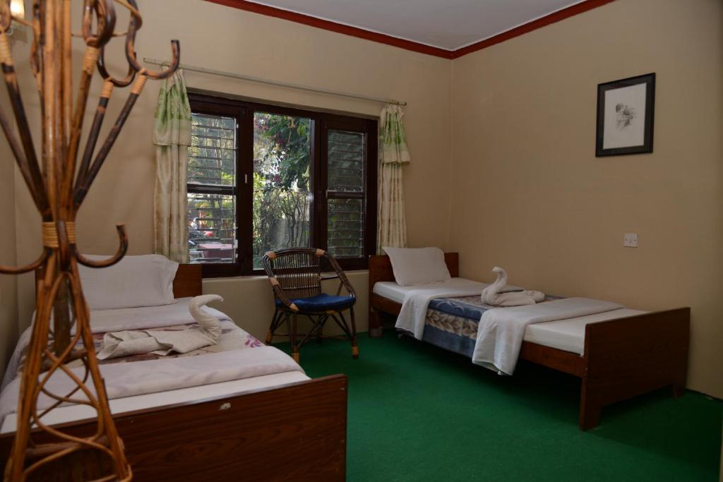 博卡拉尼泊尔小屋旅馆的客房设有两张床、一把椅子和窗户。