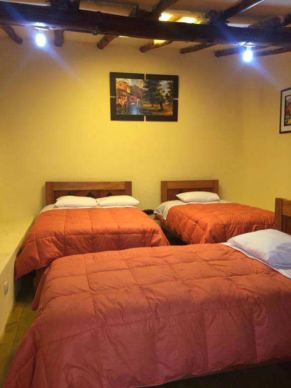 奥兰太坦波Rumi Sonqo Hostel的黄色墙壁的房间里设有三张床
