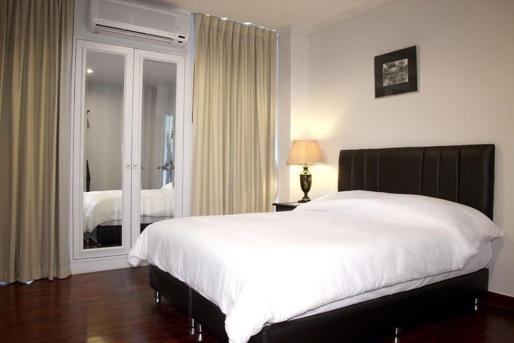 曼谷山森套房/两卧室套房公寓的卧室设有一张白色大床和一扇窗户。