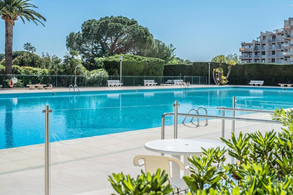 曼德琉-拉纳普勒Cannes Marina Appart Hotel Mandelieu的大楼前的游泳池配有桌椅