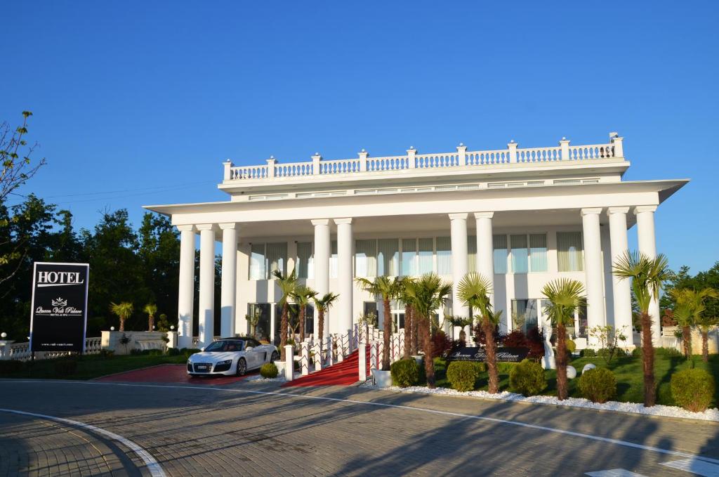 PrilepnicaQueen Vali Palace的一座白色的大建筑,前面有停车位