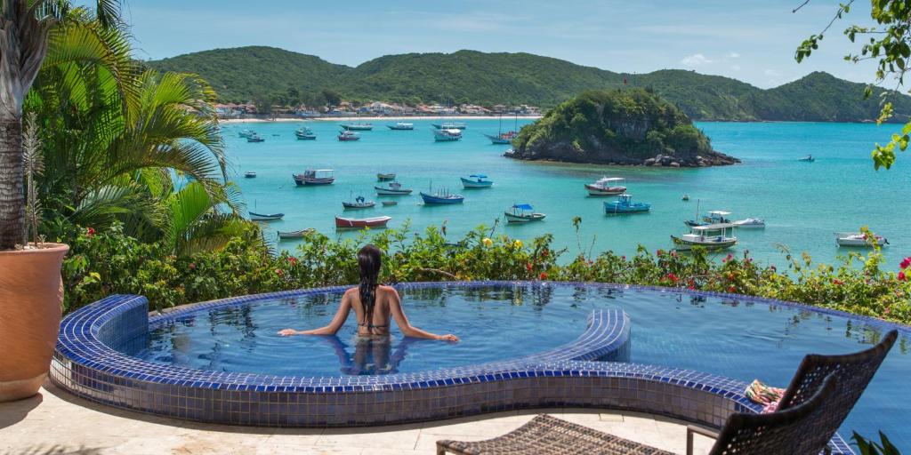 布希奥斯Vila deste Hotel的坐在俯瞰大海的小型游泳池中的女人