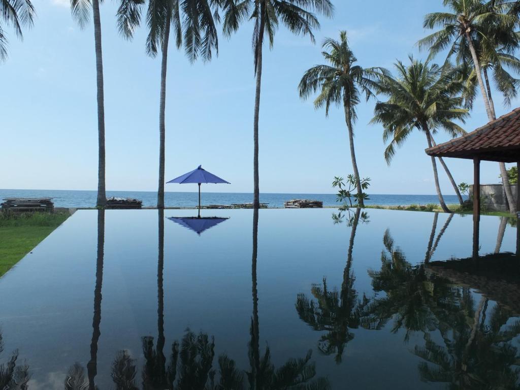 特贾库拉阿姆瑞塔盐田别墅旅馆的一个带棕榈树和遮阳伞的无边泳池