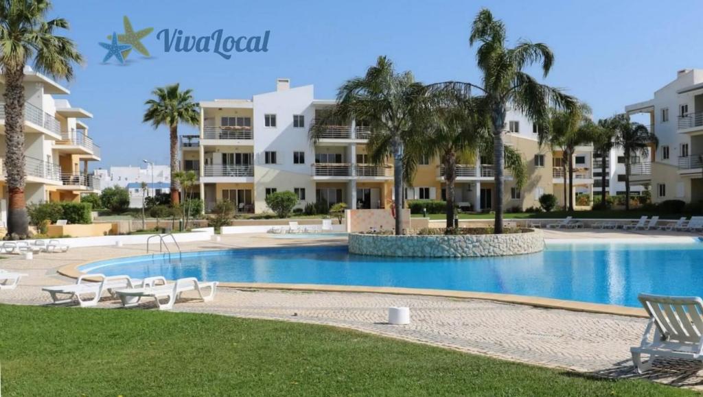 阿尔沃尔Vila da Praia - Apartamento Viva Local的棕榈树和建筑度假村内的游泳池