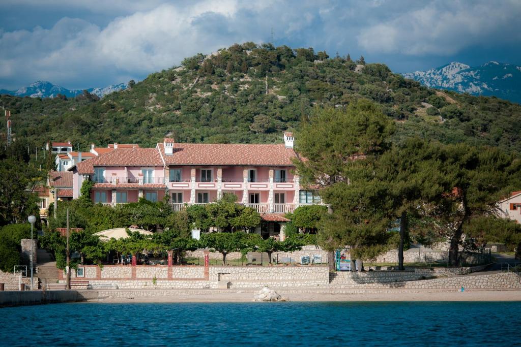 拉布Hotel Villa Barbat的水体旁的山丘上一座粉红色的大建筑