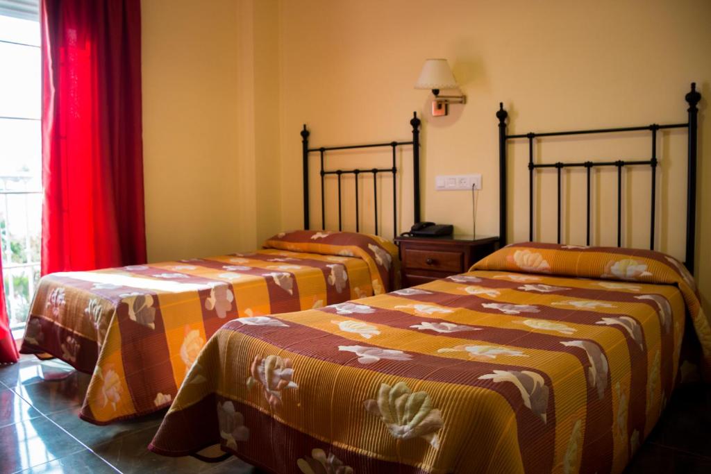 阿德拉Hostal Restaurante La Curva的配有红色窗帘的客房内的两张床