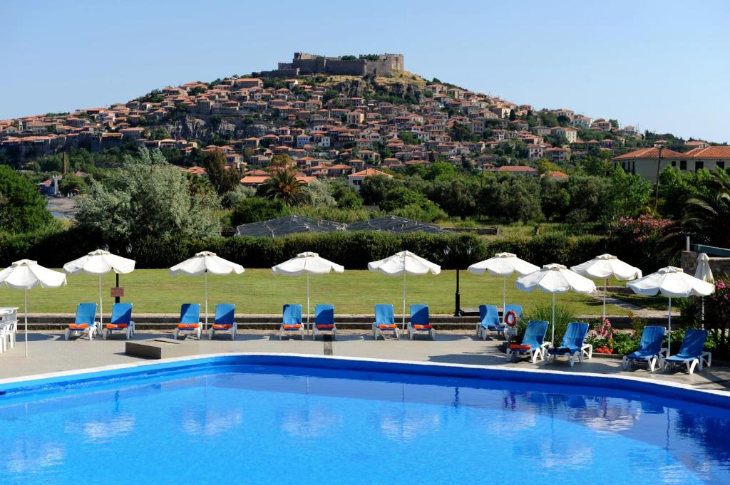 米西姆纳Delfinia Hotel & Bungalows的一个带椅子和遮阳伞的游泳池以及一座小山