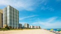 默特尔比奇Hilton Grand Vacations Club Ocean 22 Myrtle Beach的海滩上设有椅子和遮阳伞,还有建筑