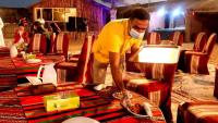 迪拜Overnight Chalet Campsite best for Couples Friends Parties and Overnight Event的蒙面人把商店里的桌子打扫干净