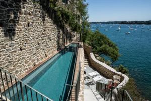 迪纳尔Castelbrac Hotel & Spa的水边石墙旁边的游泳池