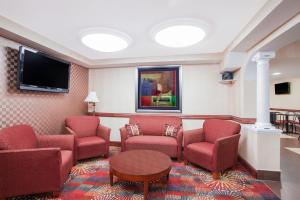 埃奇伍德Ramada by Wyndham Edgewood Hotel & Conference Center的一间设有红色椅子和平面电视的等候室