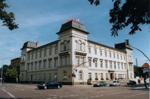 克滕Hotel "Stadt Köthen"的一座白色的大建筑,前面有汽车停放