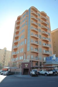 科威特Terrace Furnished Apartments Fintas 2的一座高大的建筑,前面有汽车停放