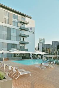 比勒陀利亚缅因门林首都酒店的一座带椅子和遮阳伞的游泳池位于一座建筑旁边