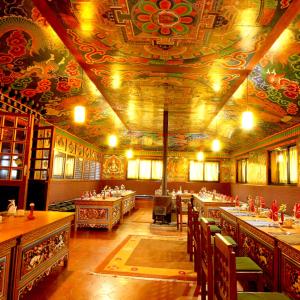 LuklaMountain Lodges of Nepal - Lukla的餐厅设有桌椅和天花板绘画作品