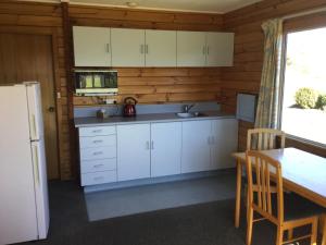 WetheralKairaki Beach Motor Camp的厨房配有白色橱柜、桌子和冰箱。