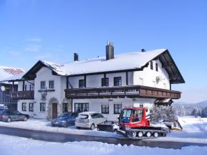菲利普斯罗伊特Pension Philippsreut "Zum Pfenniggeiger"的前面有拖拉机,有雪盖的房子