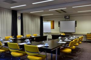 埃因霍温Onderwijshotel De Rooi Pannen Eindhoven的一间会议室,配有桌子、黄色椅子和屏幕