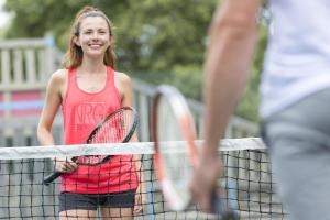 波讷地区圣朱利安Camping Officiel Siblu Les Dunes de Contis的站在网球场上,手持球拍的年轻女孩