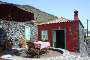 丰卡连特德拉帕尔马Casa Rural La Caldera的红色的房子,配有桌子和雨伞