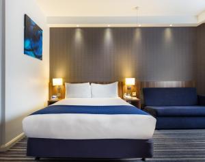 科尔切斯特快捷假日科尔切斯特酒店的一间卧室配有一张大床和一张蓝色椅子