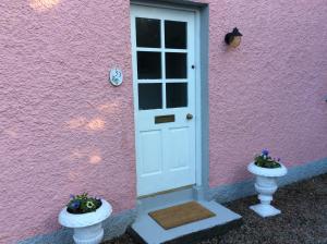 贝尔法斯特Hallmount Cottage - Belfast的粉红色的房子,有一扇白色的门和两瓶花