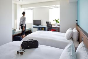 东京the b shimbashi toranomon的酒店客房设有两张床,还有人从窗户走来