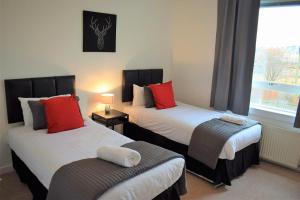 格兰奇茅斯Kelpies Serviced Apartments MacGregor- 2 Bedrooms的一间卧室配有两张带红色枕头的床和窗户。