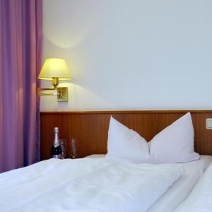 奥伊宾Naturparkhotel Haus Hubertus的一张带白色床单和一盏灯的床和一瓶