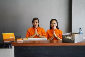 棉兰瓜拉纳穆莱夫利酒店的两个穿着橙色衬衫的女孩坐在一张桌子上,手提电脑