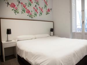 瓦伦西亚苏荷朋友公寓的卧室配有白色的床铺,墙上挂着鲜花