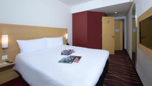 麦纳麦ibis Seef Manama的酒店客房设有一张白色大床,上面有杂志