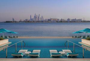迪拜The Retreat Palm Dubai MGallery by Sofitel的水边带椅子和遮阳伞的游泳池