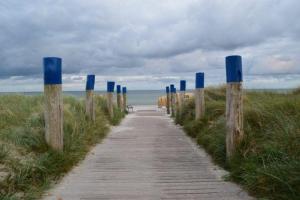 费曼城堡Ferienwohnung-am-Suedstrand的通往海滩的木道,海滩上设有蓝色的柱子
