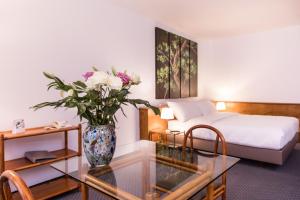 日内瓦Hotel Sagitta的一间卧室配有一张床,玻璃桌上有一个花瓶