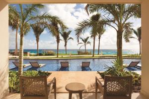 坎昆Hyatt Ziva Cancun的享有棕榈树泳池的景致,配有桌椅。