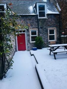 阿伯丁The Cottage的雪上设有红色门和野餐桌的房子