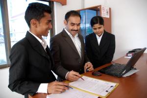 菩提伽耶菩提迦耶酒店学校的三位身着装的男士站在一张桌子旁,手提电脑