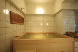 松本新站酒店的浴室铺有白色瓷砖,设有大浴缸。
