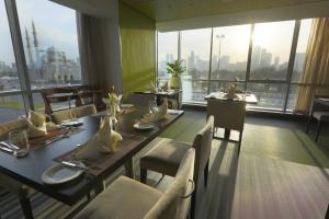 沙迦Hotel 72 Sharjah Waterfront的一间带桌椅的用餐室和大窗户