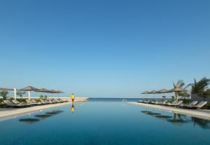 马斯喀特马斯喀特凯宾斯基酒店的一个带椅子的游泳池,背景是大海