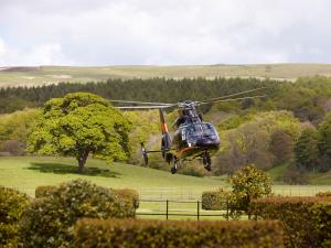 博尔顿阿比The Devonshire Arms Hotel & Spa - Skipton的一架直升飞机,用树飞越一个田野