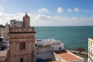 加的斯Hotel Casa de las Cuatro Torres的一座建筑,有一个钟楼,靠近大海