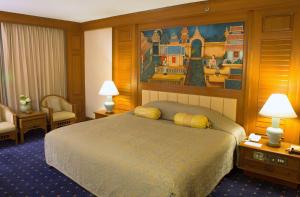 清迈清迈广场酒店的酒店客房设有一张床,墙上挂有绘画作品
