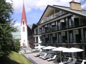 蒂罗尔-泽费尔德Alpenlove - Adult SPA Hotel的一座带椅子和遮阳伞的建筑和一座教堂