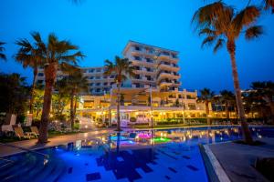 帕福斯爱美尔海滩酒店及度假中心的夜间有游泳池和棕榈树的酒店